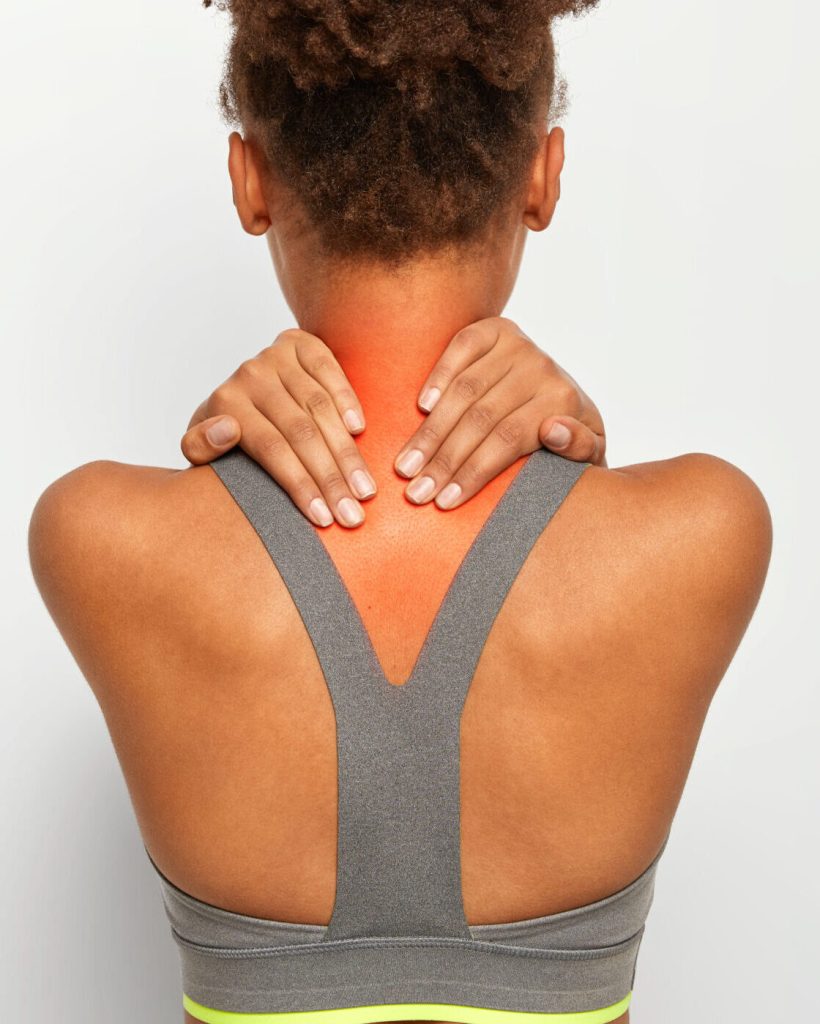 Cropped image of faceless African American woman touches neck with both hands, shows problematic zone, being injured, dressed in active wear, poses over white studio wall, blank space for text